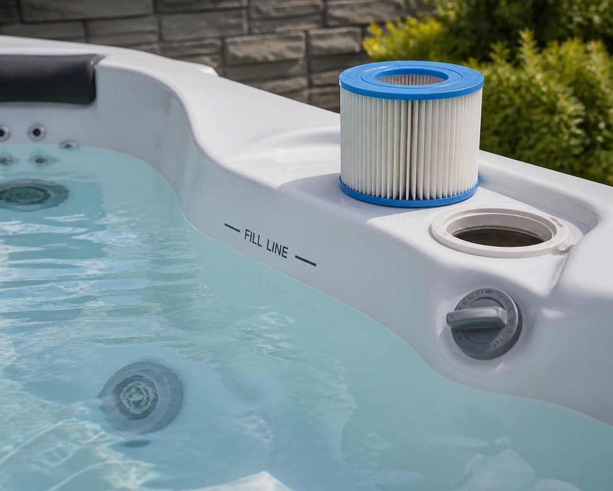 Cartouche de filtre de spa retirée et posée sur le rebord près de la ligne d'eau, d'une vanne et d'une buse d'hydromassage.