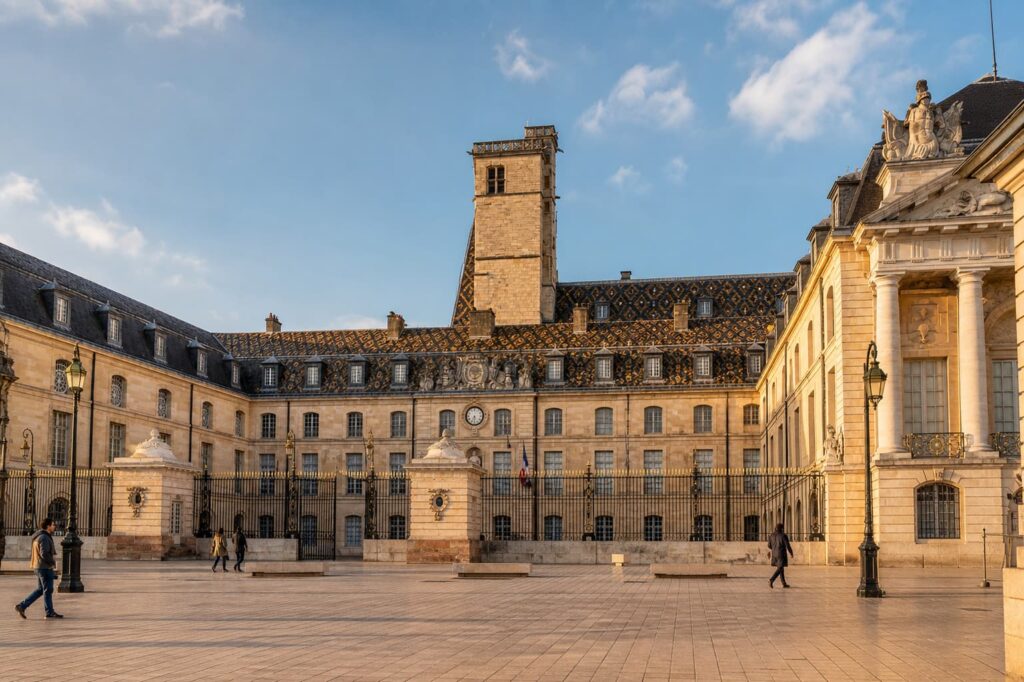 Vue de la place de la Libération avec le palais des ducs de Bourgogne en arrière-plan, sous une lumière chaude, avec quelques passants.