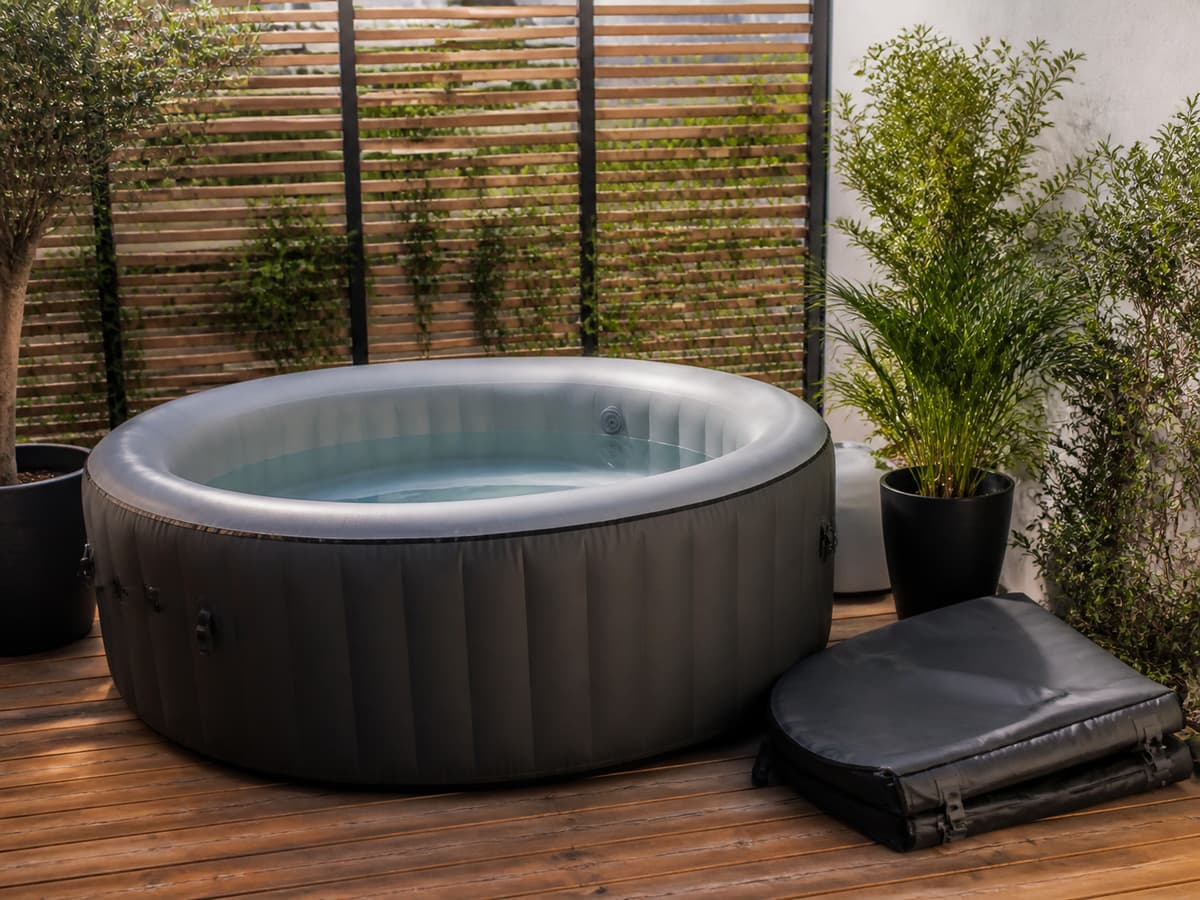 Un spa gonflable installé sur une terrasse en bois extérieure avec sa couverture de protection repliée à proximité.
