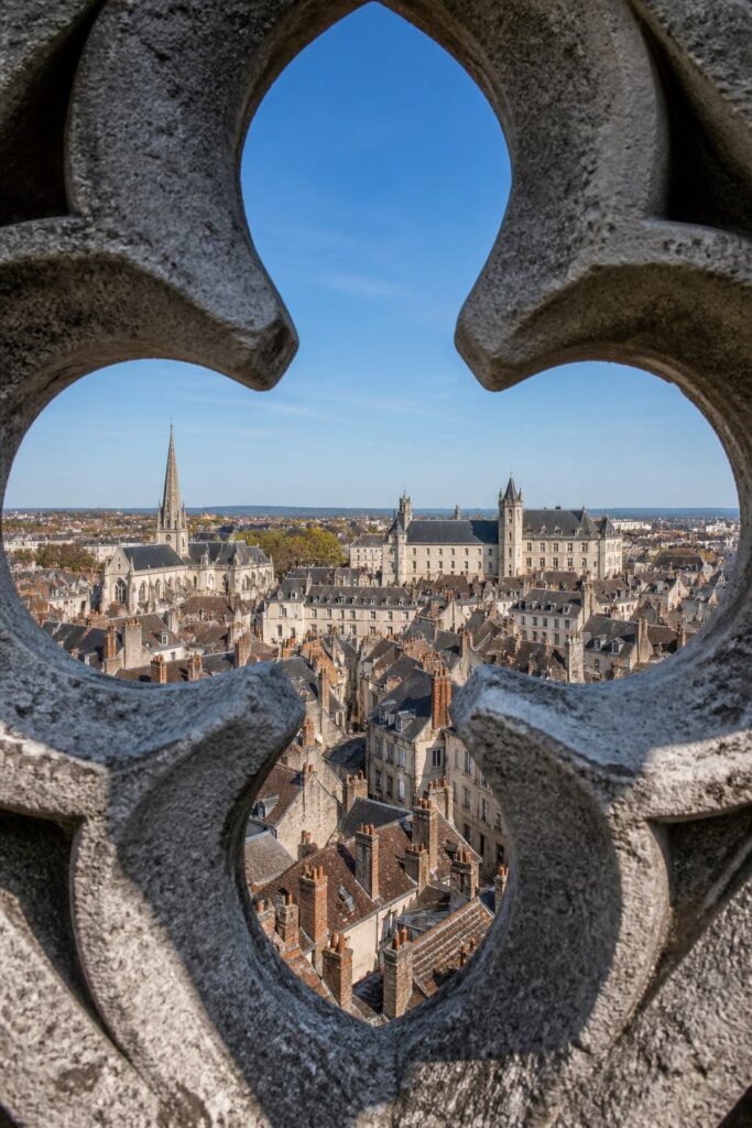 Vue panoramique depuis le sommet de la tour Philippe le Bon sur les toits de Dijon, avec le palais des Ducs de Bourgogne visible et la pierre de la tour cadrant la scène.